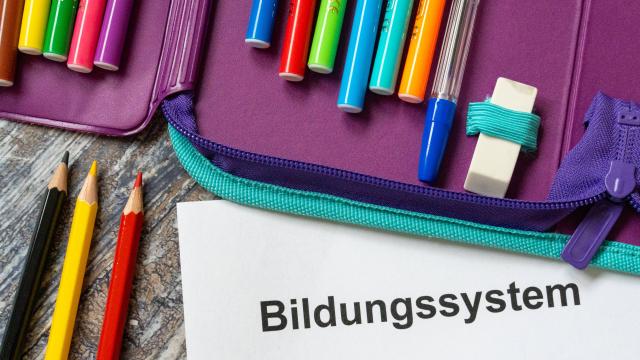 Mäppchen mit Buntstiften auf einem Tisch. Darunter ein Blatt Papier, auf dem "Bildungssystem" steht. 