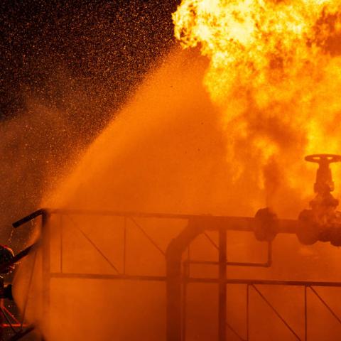 Firefighters using water fog spraying down fire from oil rig factory explosion.