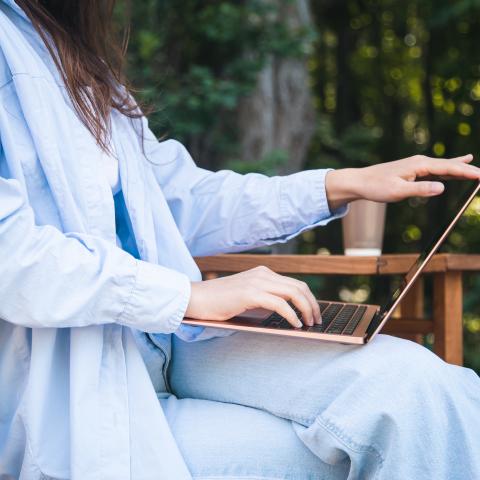 Person sitzt im Garten und hat ein Laptop auf dem Schoß