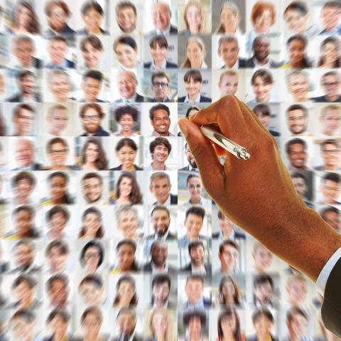 Hand von Geschäftsmann mit Stift sucht in Panorama aus Geschäftsleuten nach passender Bewerbung